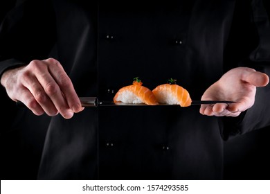 Sushi served on japanese knife in chef hands on dark background. Decorated salmon sashimi nigiri. Traditional japanese food. Copy space for text - Powered by Shutterstock