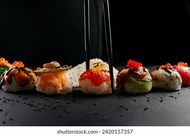 Sushi set with caviar, avocado and salmon. Sushi pieces placed between chopsticks, separated on black background. Asian cuisine. Top view. Free space for your text. High quality photo
