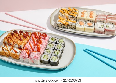 Sushi set on ceramic dishware with coloured chopsticks. Trendy set of maki sushi in minimal style. Modern japanese menu concept. Maki sushi assorted on coloured background - Shutterstock ID 2146133933