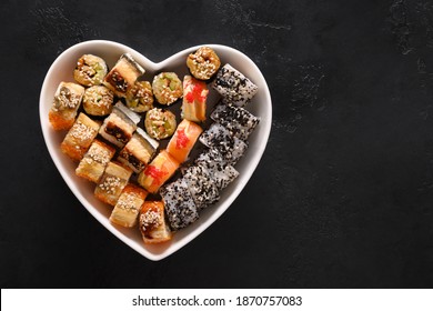 Sushi set in plate as heart on black background. Valentine's day food love concept. View from above. Space for text. Flat lay style.