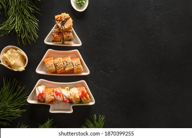 Sushi set served on plate as Christmas tree with Xmas decoration on black background. View from above. Space for text. Flat lay style.