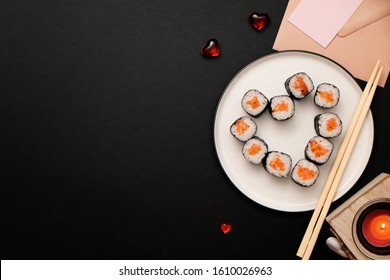 Sushi for Valentines Day - roll in heart shape, on plate on black background. Flat lay. Space for text.
