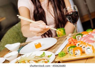 Sushi. Woman hand with Japanese sticks.. Sushi set at plate on wood table.