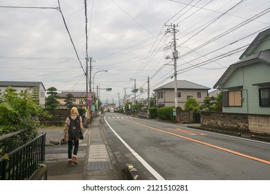 Susono, Japan - May 2014: Perspective View Of Empty Main Road In Small Town With Houses And Electrical Network Cable Post Along Road And Cloudy Blue Sky Background. A Woman Walking On Sidewalk.