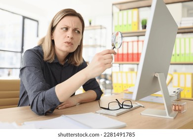Suspecting woman with magnifying glass seeks information on internet in office closeup. Fact checking to find trustful online sources