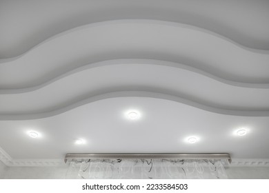 suspended ceiling with halogen spots lamps and drywall construction  with intricate crown molding in empty room in apartment or house. Stretch ceiling white and complex shape.