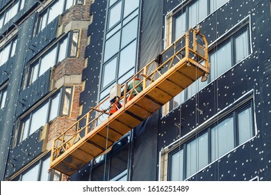 Suspended construction craddle near wall of hightower residentaial building with insulation and ventilated facade on construction site. Engineering urban background