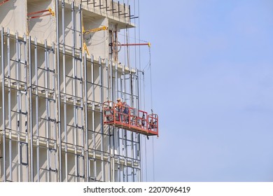 Suspended construction cradle on white facade of building with workers.