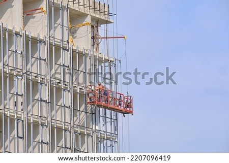 Suspended construction cradle on white facade of building with workers.