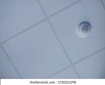 Suspended (drop) Ceiling Of T-bar Grid With Textured White Tiles (acoustic Panels) And Motion Sensor In Angular View In Office Building