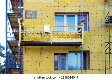 Suspended motor scaffolding platform on facade of residential building under renovation. High-altitude works, wall thermal insulation with mineral wool. - Shutterstock ID 2138014049