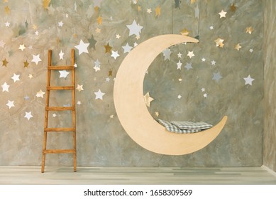 Suspended swing in the shape of the moon on a gray background with stars.