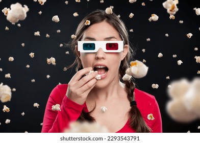 Suspenseful films galore. Shot of a young woman wearing 3D glasses and eating popcorn against a studio background. - Powered by Shutterstock