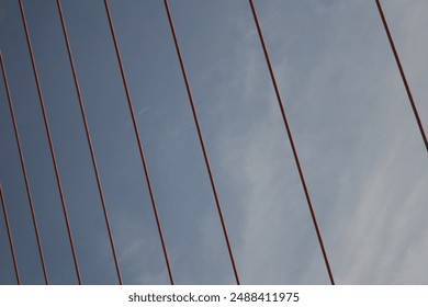 suspension bridge against a clear blue sky. The bridge has two towers that support a network of red cables.  - Powered by Shutterstock