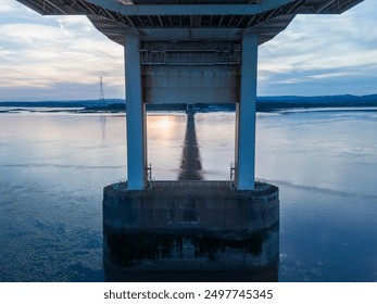 Suspension bridge concrete support standing in calm water at sunset - Powered by Shutterstock