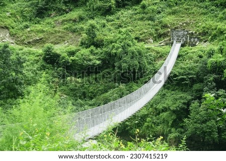 A suspension bridge gracefully complements the lush Himalayan rainforest on the Manaslu Circuit trek in Nepal, offering a picturesque view from above.