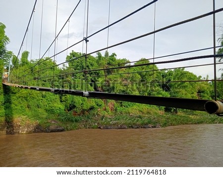 suspension bridge made of thin iron plates with colorful strong chains connecting 2 villages that were cut off by a river