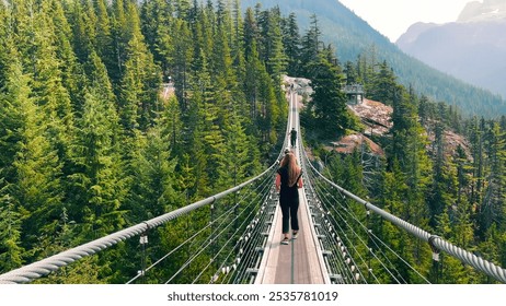 Suspension bridge over a forested valley. A long suspension bridge stretches across a lush, forested valley, with people walking across, surrounded by tall evergreen trees. - Powered by Shutterstock