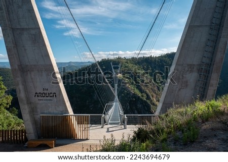 Suspension bridge over the Paiva river with concrete support pillars on which one has the inscription in Portuguese of 