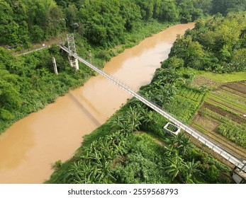 Suspension Bridge Over Rural Farmland and River Surrounded by Lush Greenery - Powered by Shutterstock