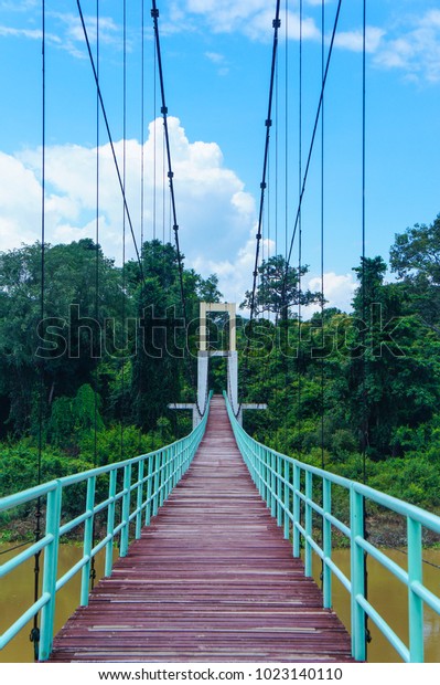 Suspension bridge with wooden bridge crossing\
the river in the forest which has yellowish water under the bridge\
with bright blue sky in background, Tana Isle National Park, Ubon\
Ratchathani,\
Thailand