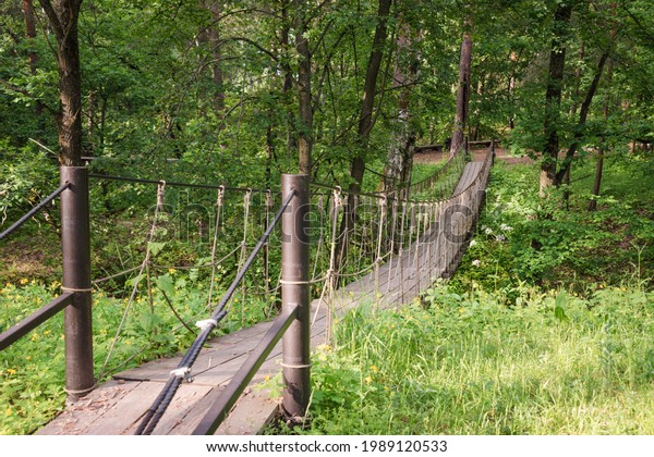 Suspension wooden bridge in the\
forest. Rope bridge suspended between two hills in the\
woods.