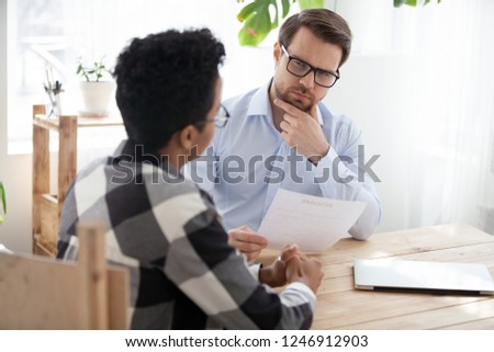 Suspicious male employer look at African American millennial applicant, doubt in candidature, thoughtful HR manager consider resume hesitating about black candidate experience at office interview