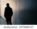 Suspicious man. Silhouette of criminal. Stalker or anonymous stranger. Gang crime, teenage gangster or thief. Dark urban street alley. Face hidden in shadow. Scary figure at night. Grunge background.