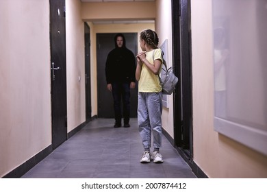 Suspicious man spying on entrance. space for text. Child in danger. frightened caucasian child girl is alone indoors, having no help, looking back. child abuse, pedophilia, maniac, violence, crime