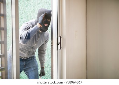 Suspicious Man Wearing A Ski Mask And Carrying A Plank Looking Through A Glass Door