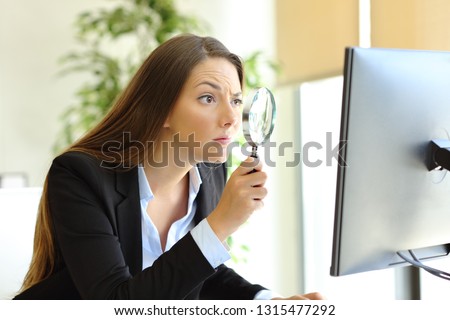 Suspicious office worker checking online content on computer using a magnifying glass