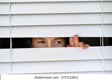 Suspicious Person Looking Outside Home Window From Behind Venetian Curtains. Concept Photo Of Person That Have Pistanthrophobia And Agoraphobia, A Person Who Don't Trust Fear Of Leaving The House. 