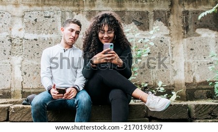 Suspicious person spying on his girlfriend phone, Jealous guy spying on his girlfriend phone, Distrustful boyfriend spying on his girlfriend phone
