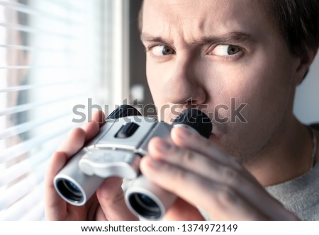 Suspicious, skeptic and confused man with binoculars. Conspiracy theory, paranoia, skepticism or suspicion concept. Curious or paranoid person looking out the window. Mistrustful and nervous guy.
