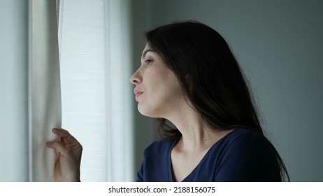 Suspicious Woman Standing By Window Looking Outside. Person Seeing Through Curtains