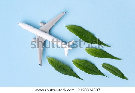 Sustainable Aviation Fuel. White airplane model, fresh green leaves on blue background. Clean and Green energy, Biofuel for aviation industry.
