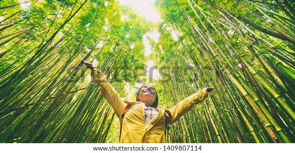 Sustainable eco-friendly travel\
tourist hiker walking in natural bamboo forest happy with arms up\
in the air enjoying healthy environment renewable\
resources.