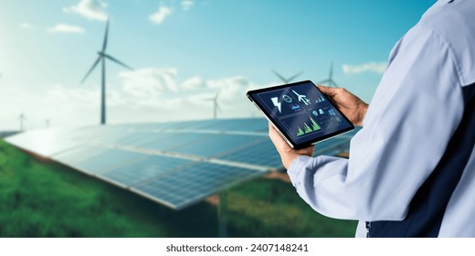 Sustainable energy management system concept.Engineer using digital tablet with wind turbine and solar panels powerplant as background - Powered by Shutterstock