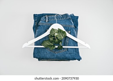 Sustainable Fashion, Circular Economy, Denim Eco Friendly Clothing. Green Leaf Plant And Wooden Clothes Hanger On Blue Denim Jeans Background