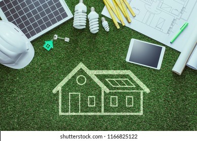 Sustainable House Projects And Green Building Concept: Blueprint, Solar Panel And Tools On Lush Grass