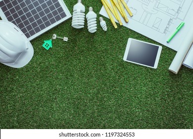 Sustainable house projects and green building concept: blueprint, solar panel and tools on lush grass