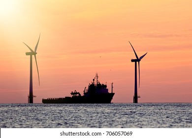 Sustainable resources. Wind farm with ship silhouette at tropical sunrise or sunset. Solar and wind energy and food supply represented in this tranquil image with copy space.