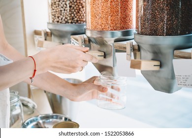 Sustainable shopping at small local businesses. Close-up image of woman pours red lentils in glass jar from dispensers in plastic free grocery store. Girl with cotton bag buying in zero waste shop. - Powered by Shutterstock