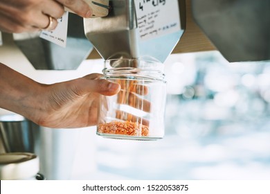 Sustainable shopping at small local businesses. Close-up image of woman pours red lentils in glass jar from dispensers in plastic free grocery store. Girl with cotton bag buying in zero waste shop.
