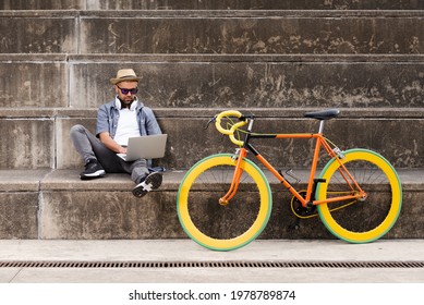 Sustainable transport and technology concept. Hispanic freelancer working on his laptop beside a colorful fixie bike.