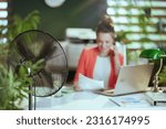 Sustainable workplace. Closeup on happy modern woman worker at work with electric fan and laptop.