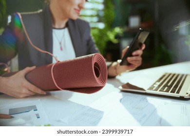 Sustainable workplace. Closeup on modern small business owner woman in modern green office with yoga mat using smartphone app. - Powered by Shutterstock