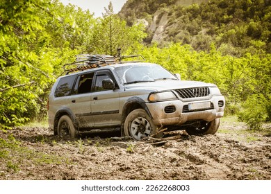 SUV 4WD grey car stuck in muddy off-road. Closeup the wheel rotates in the mud. Adventure travel Vashlovani safari tour