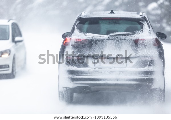 SUV car\
driving on snowy slippery road inside the forest, having\
registration number insivisible due to\
snow.