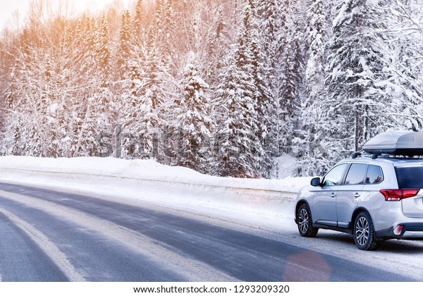 Suv car with rooftop cargo carrier trunk stay\
on roadside of winter road. Family trip to ski resort. Winter\
holidays adventure. car on winter\
road